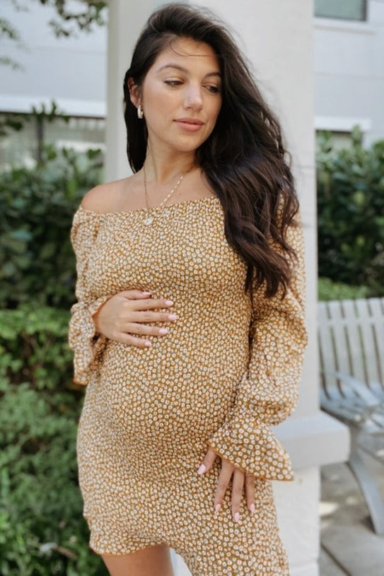 woman wearing a brown floral off-the-shoulder maternity dress and holding her baby bump