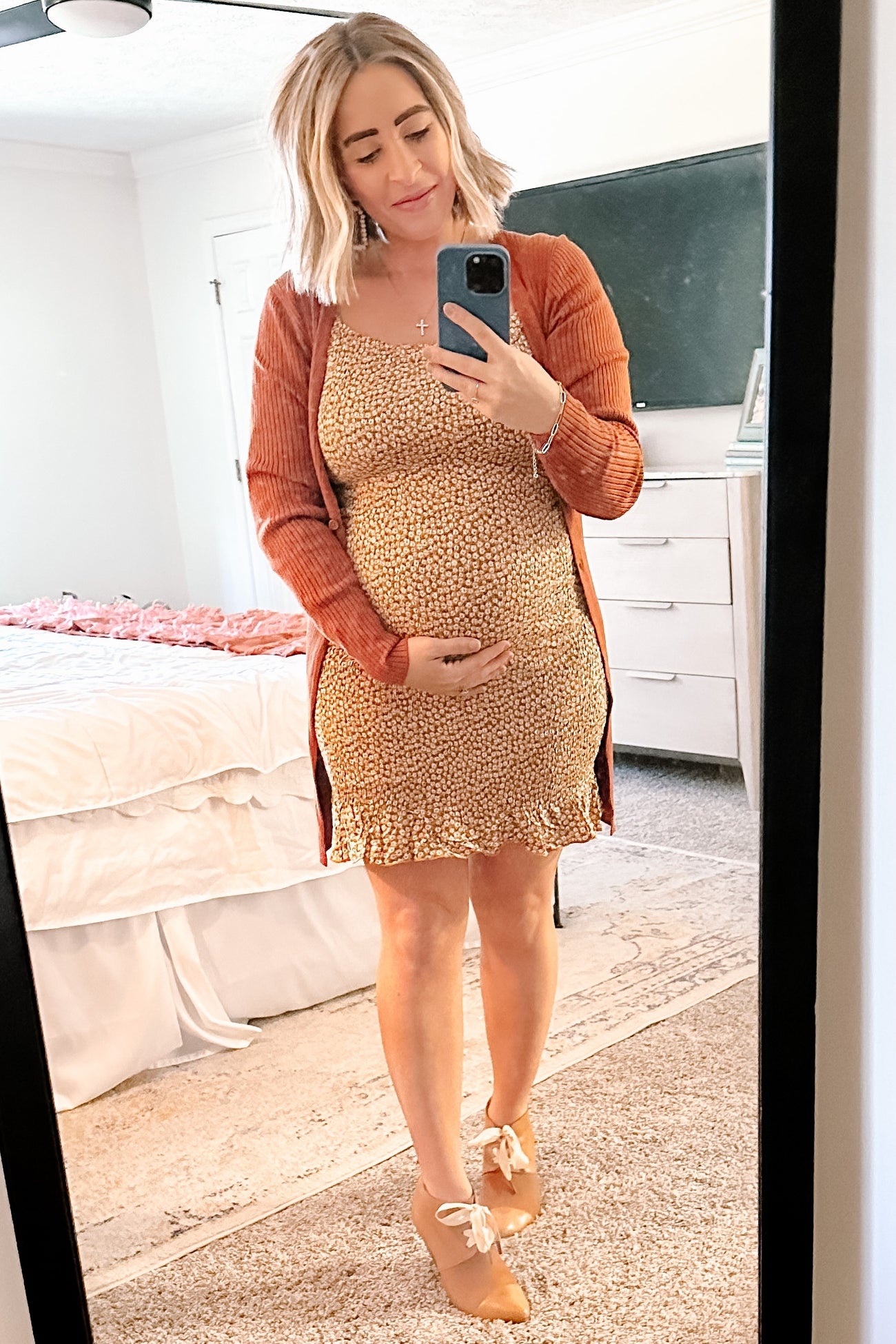 woman wearing a brown cardigan over a floral maternity dress while holding her baby bump