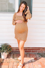 woman wearing a mustard yellow floral maternity dress and holding her baby bump outside a house