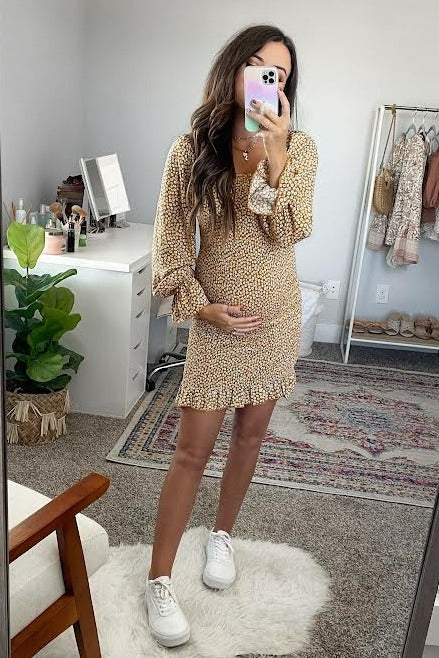 woman wearing a brown floral maternity dress with bell sleeves and holding her baby bump
