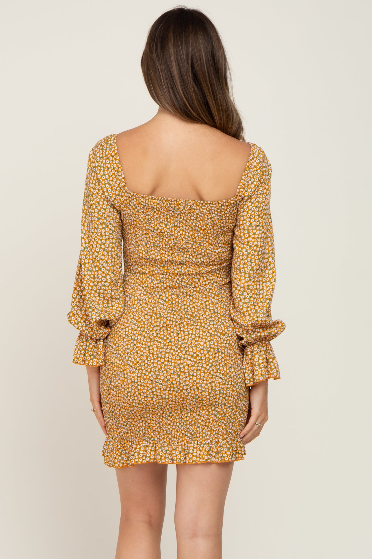 woman wearing a mustard floral print maternity dress with long sleeves and a fitted silhouette
