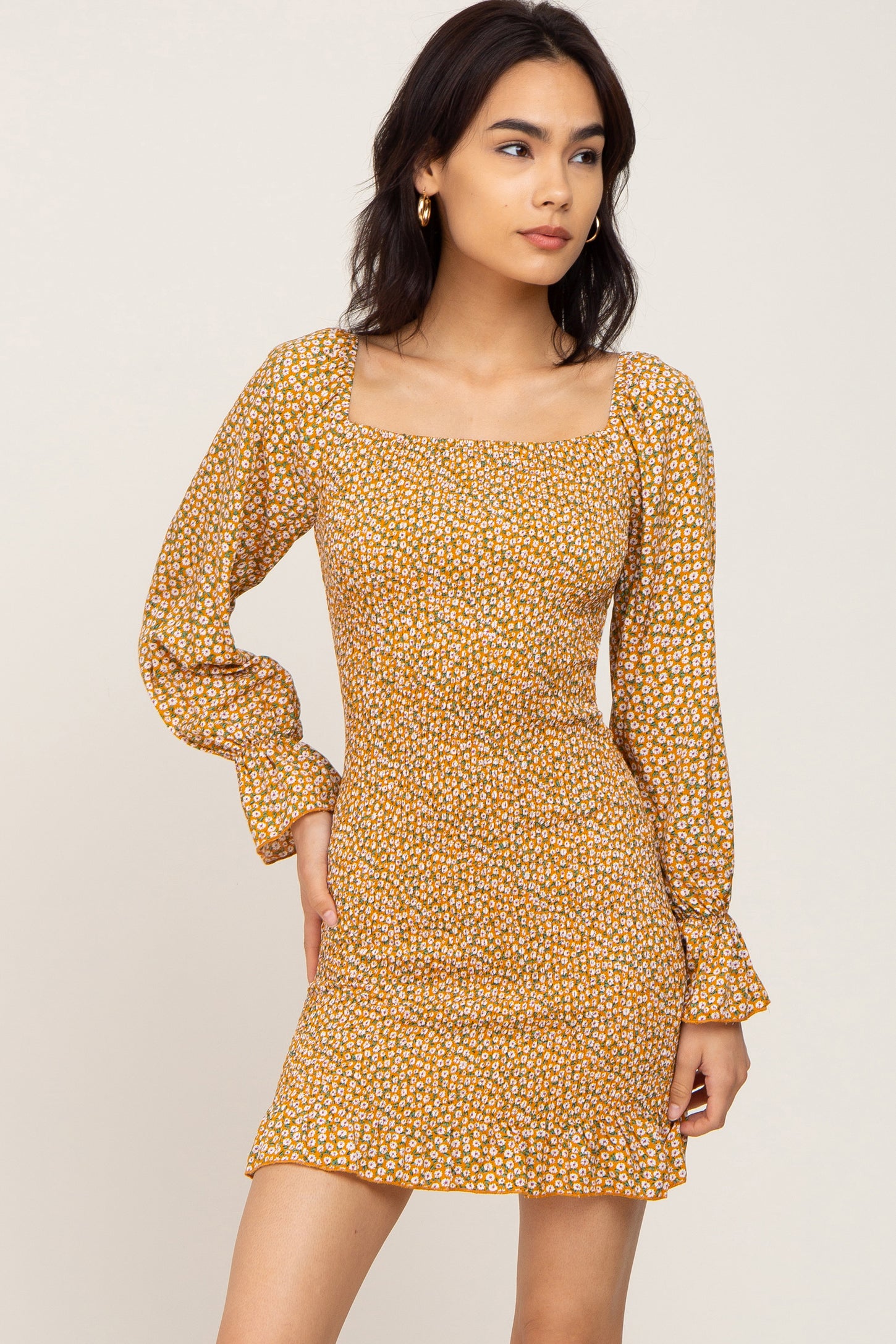 woman wearing a yellow floral long sleeve dress with a square neckline and ruffled hemline