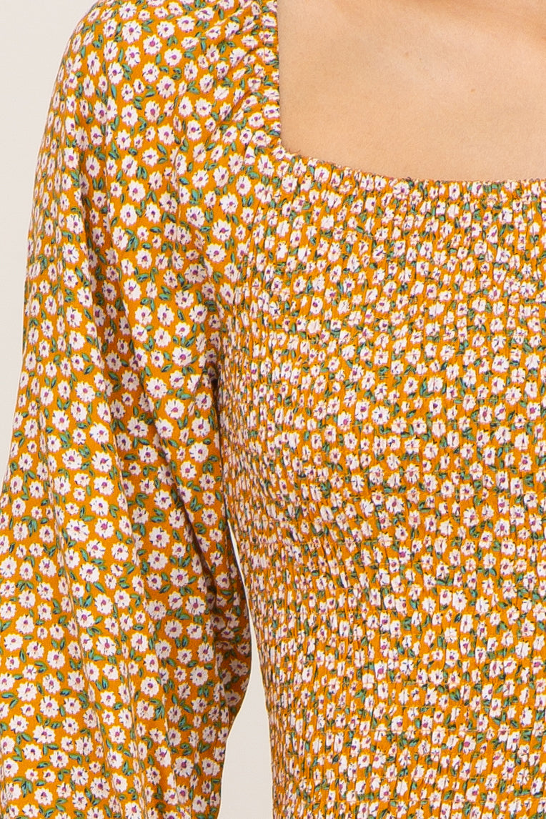 close-up of a woman wearing an orange floral smocked dress with a square neckline and bell sleeves