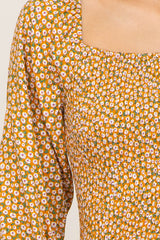 close-up of a woman wearing an orange floral smocked dress with a square neckline and bell sleeves