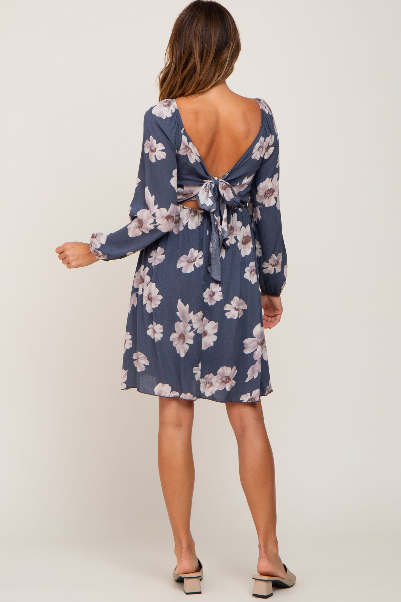 woman wearing a navy floral print dress with a tie back detail and long sleeves