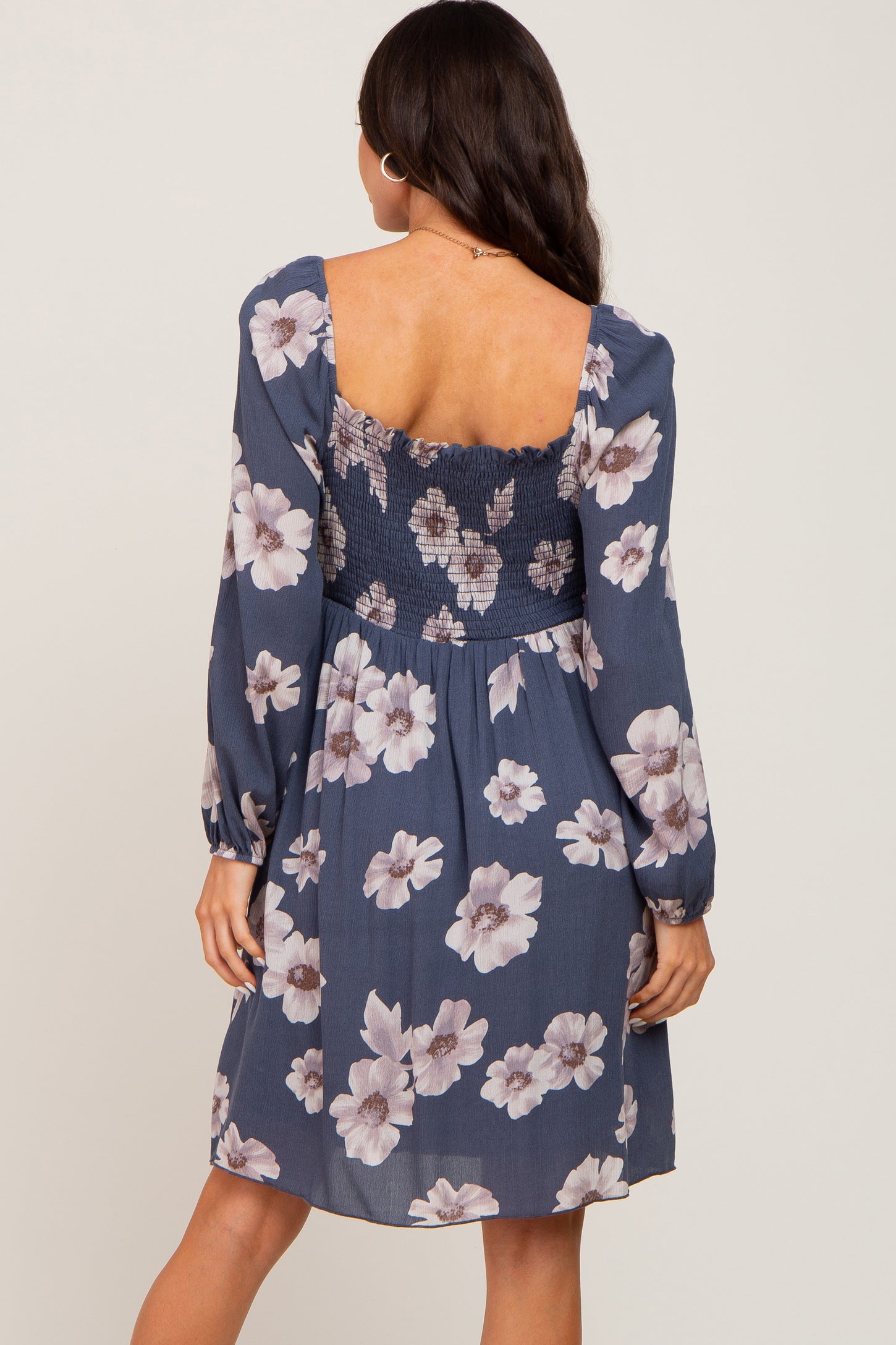 woman wearing a navy floral maternity dress with a smocked bodice and long sleeves, showing off her baby bump