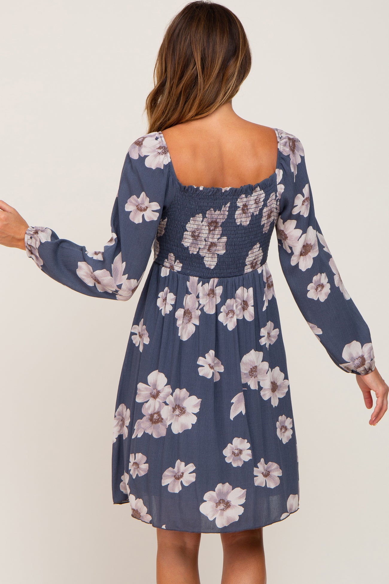 back view of woman wearing blue floral long sleeve dress with smocked back and square neckline