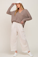 woman wearing a taupe button-up ribbed cardigan with cream wide-leg pants and a white cap