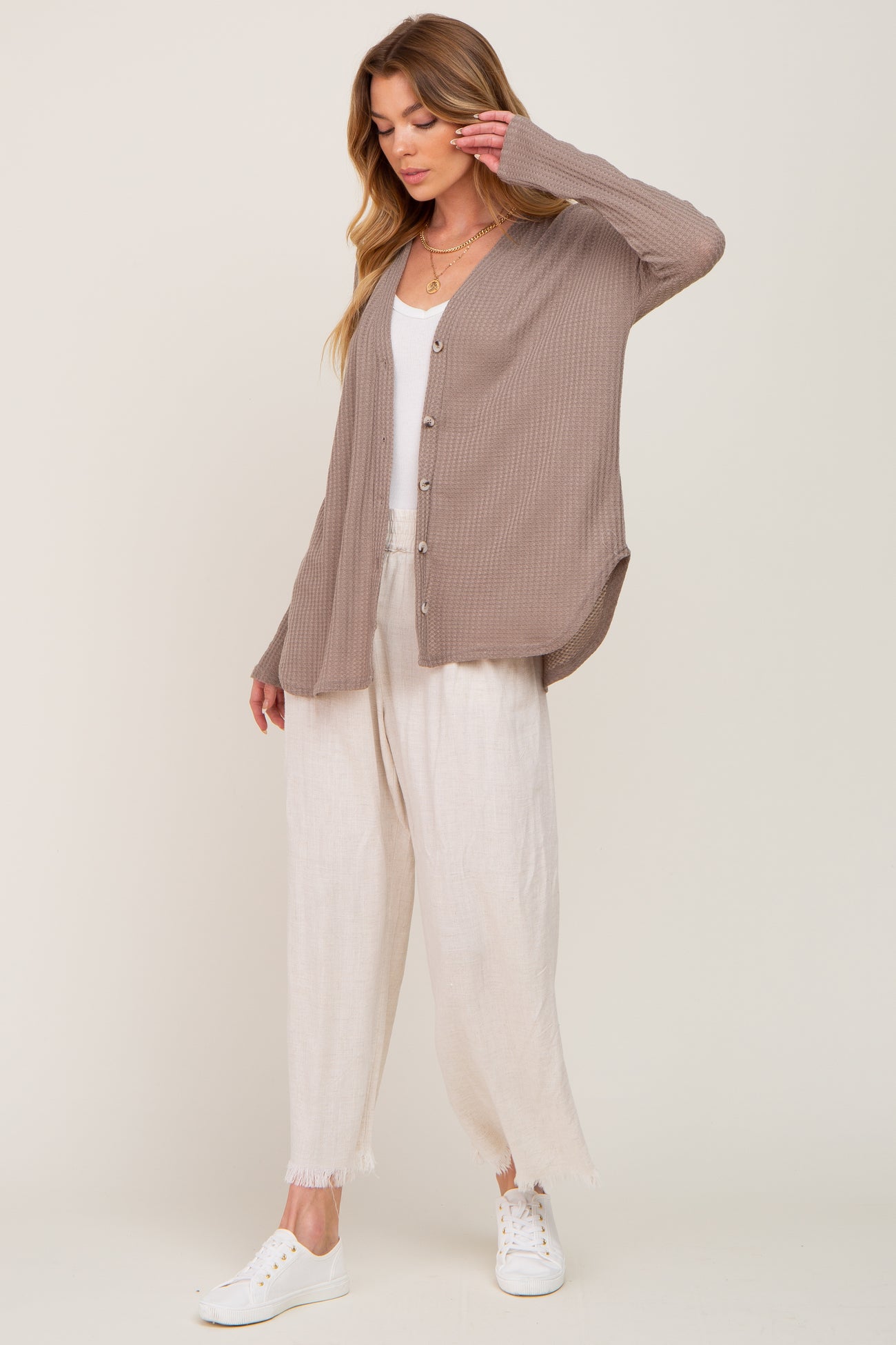 woman wearing a beige ribbed cardigan over a white tank top and light linen pants, styled with white sneakers