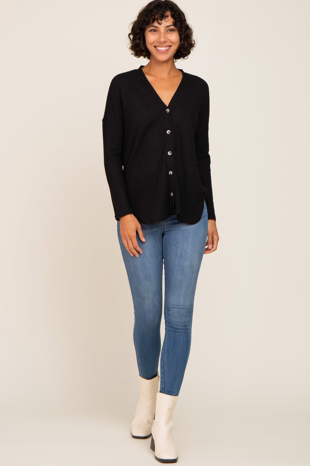 woman wearing a black ribbed button-up cardigan with long sleeves and blue skinny jeans, smiling while standing
