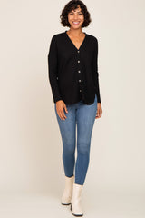 woman wearing a black ribbed button-up cardigan with long sleeves and blue skinny jeans, smiling while standing