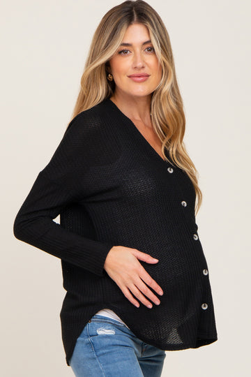 woman wearing a black maternity cardigan with buttons, posing with her baby bump visible, paired with light blue jeans