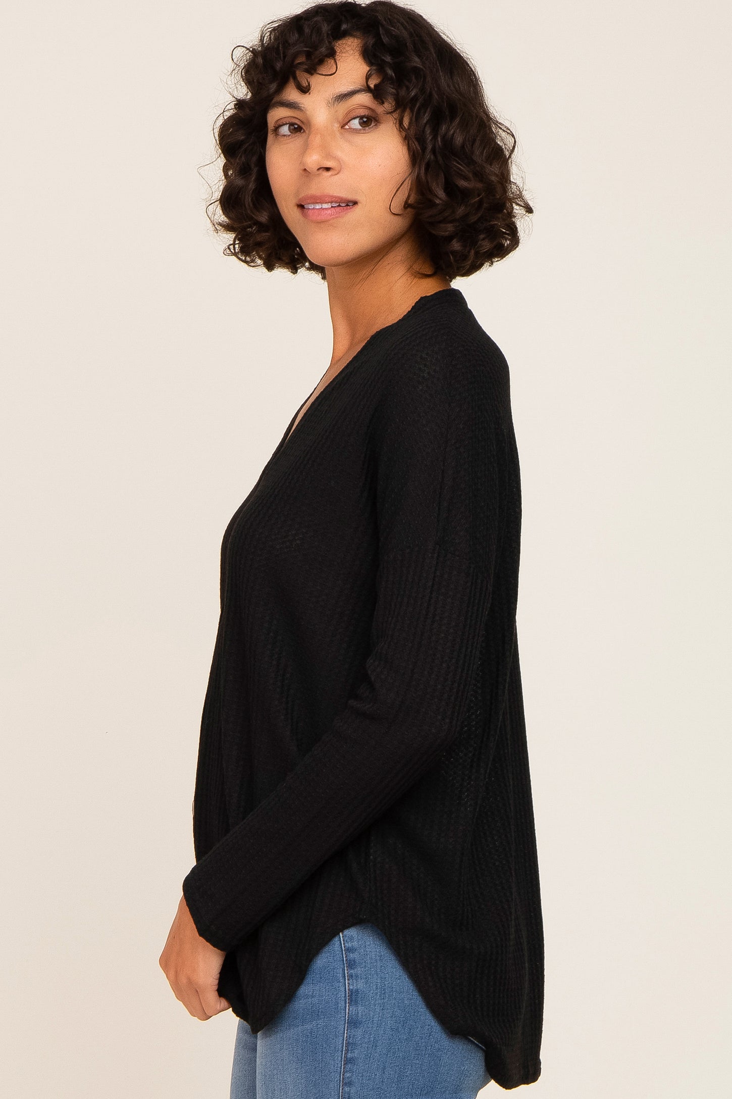 woman wearing a black long sleeve knit top with a v-neckline and relaxed fit, styled with blue jeans