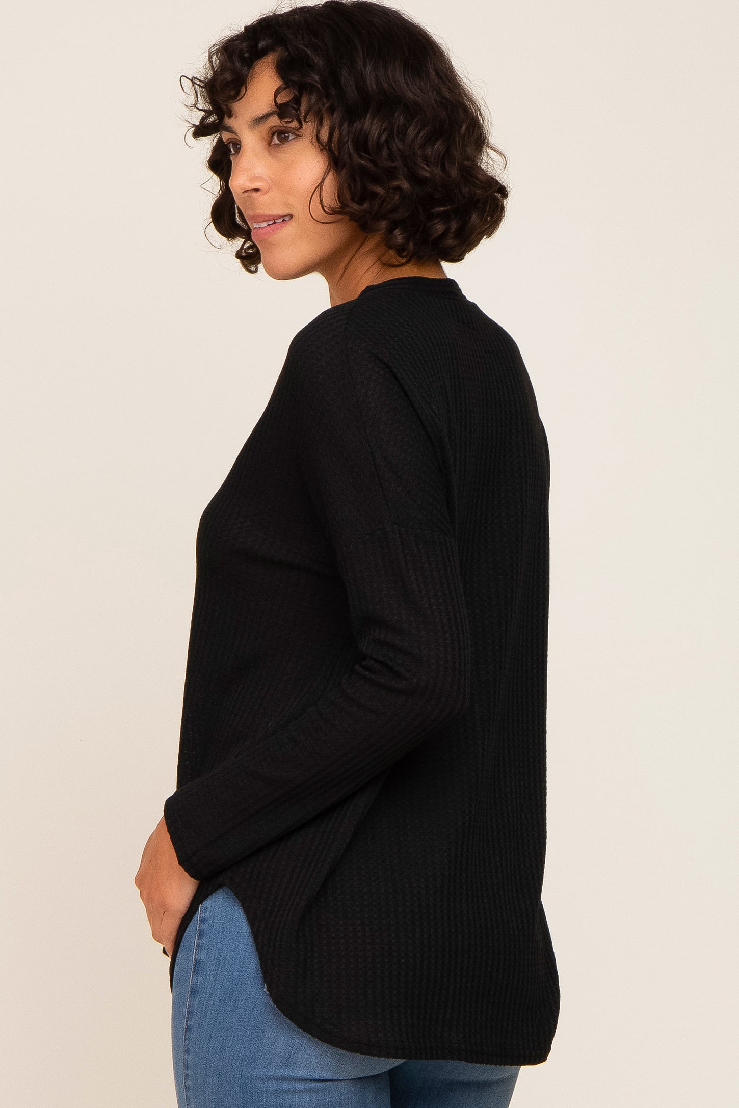 woman wearing a black long sleeve textured top with a relaxed fit and side slits, styled with blue jeans
