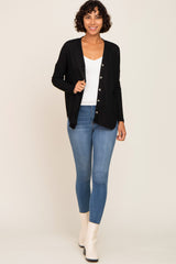 woman wearing a black ribbed cardigan over a white top and blue skinny jeans, paired with white ankle boots
