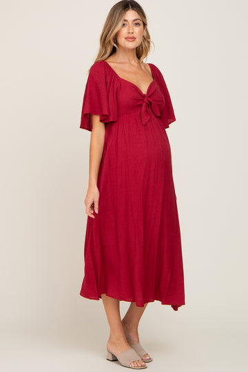 pregnant woman wearing a red maternity midi dress with flutter sleeves and a front tie detail