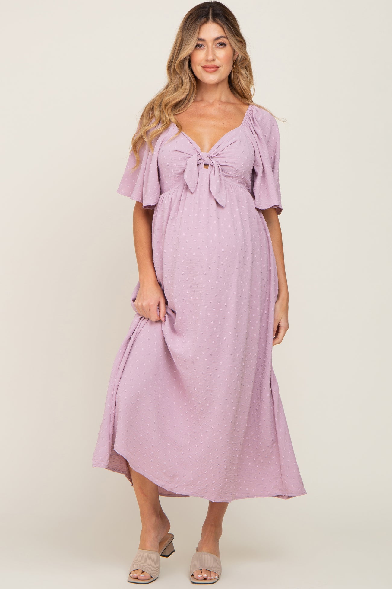 woman wearing a lavender maternity dress with a tie front and flutter sleeves, showing her baby bump