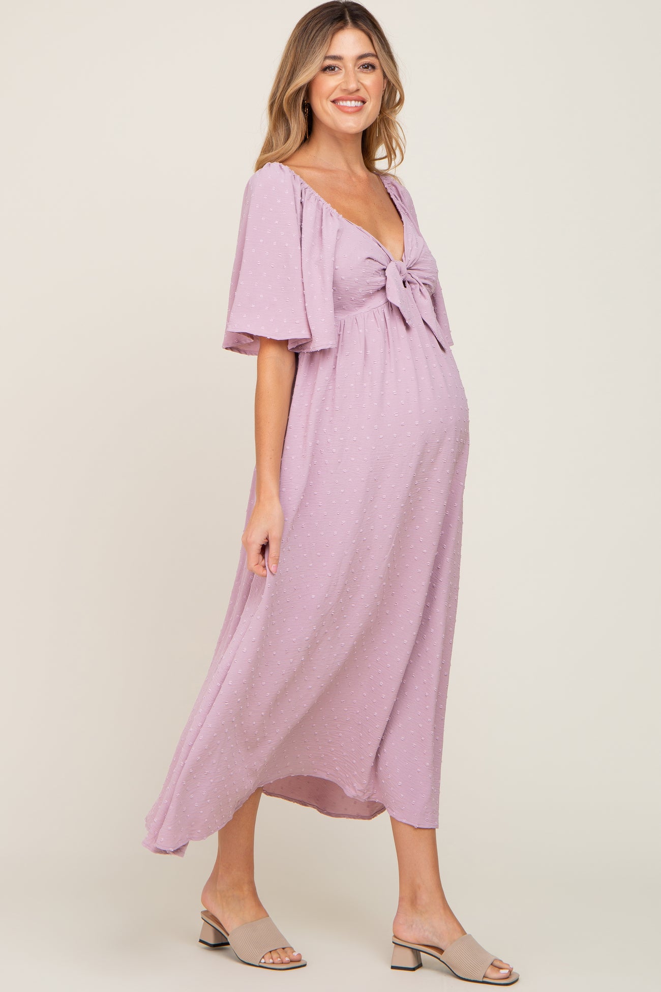 woman wearing a lavender maternity dress with a knot detail at the bust and flutter sleeves, showcasing her baby bump