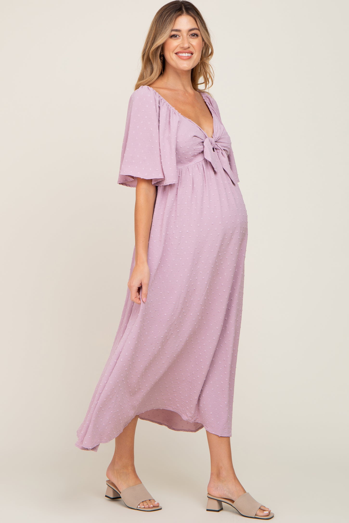 woman wearing a lavender maternity dress with a knot detail at the bust and flutter sleeves, showcasing her baby bump