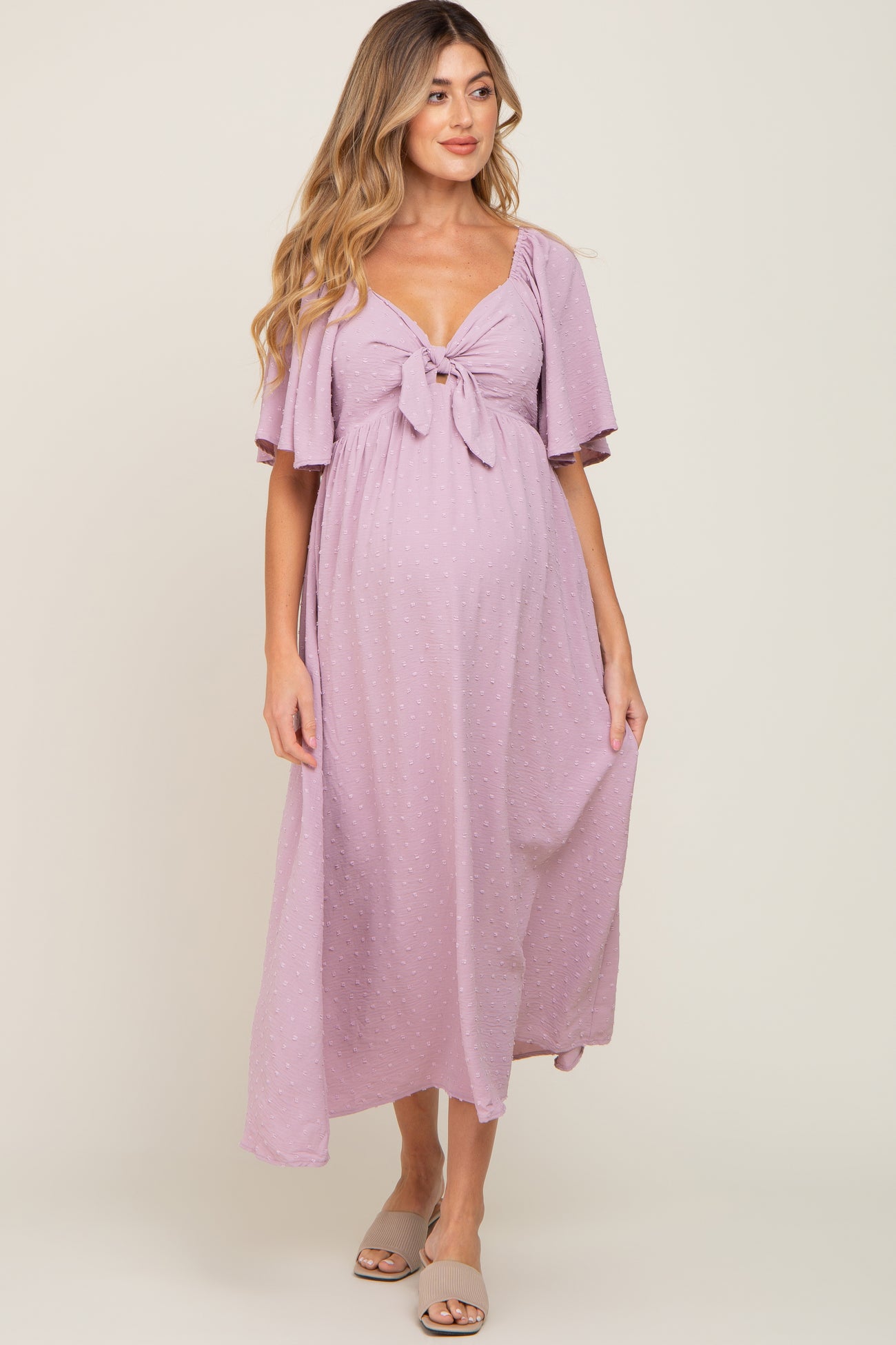 woman wearing a light purple maternity maxi dress with short flutter sleeves and a front tie detail, showing her baby bump
