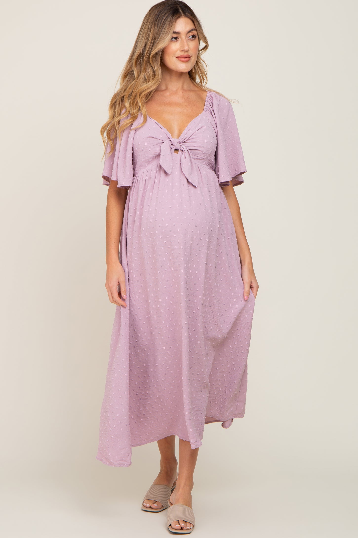 woman wearing a light purple maternity maxi dress with short flutter sleeves and a front tie detail, showing her baby bump