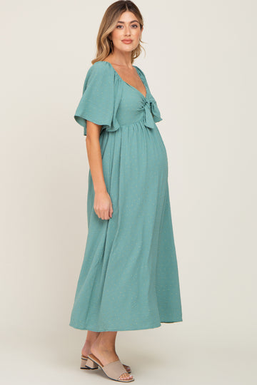 woman wearing a teal maternity dress with flutter sleeves and a tied waist, showcasing her baby bump