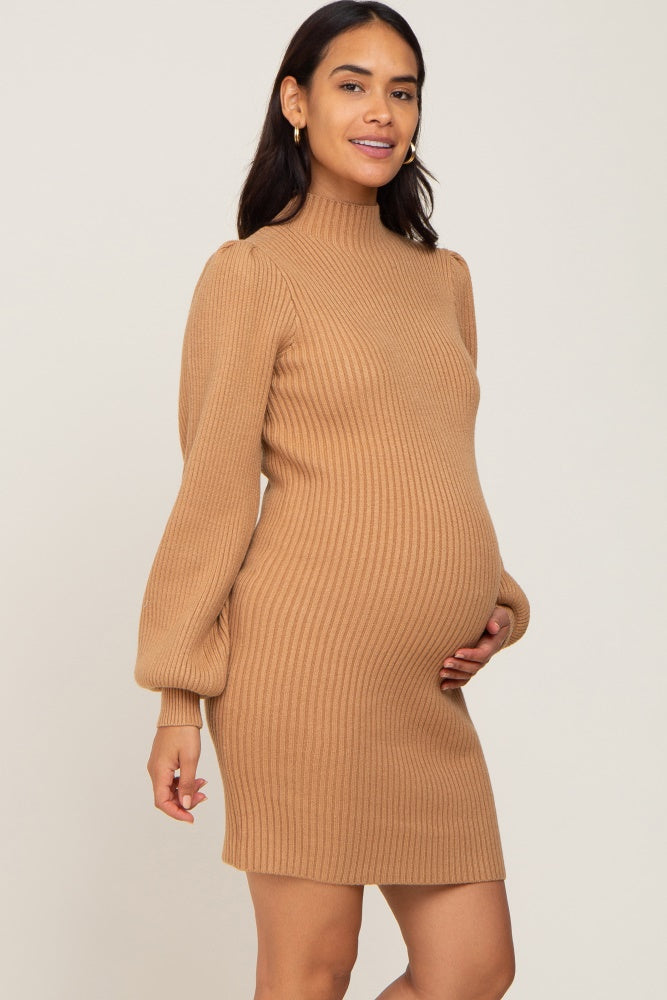woman wearing a tan ribbed maternity sweater dress with a high neckline and balloon sleeves, holding her baby bump