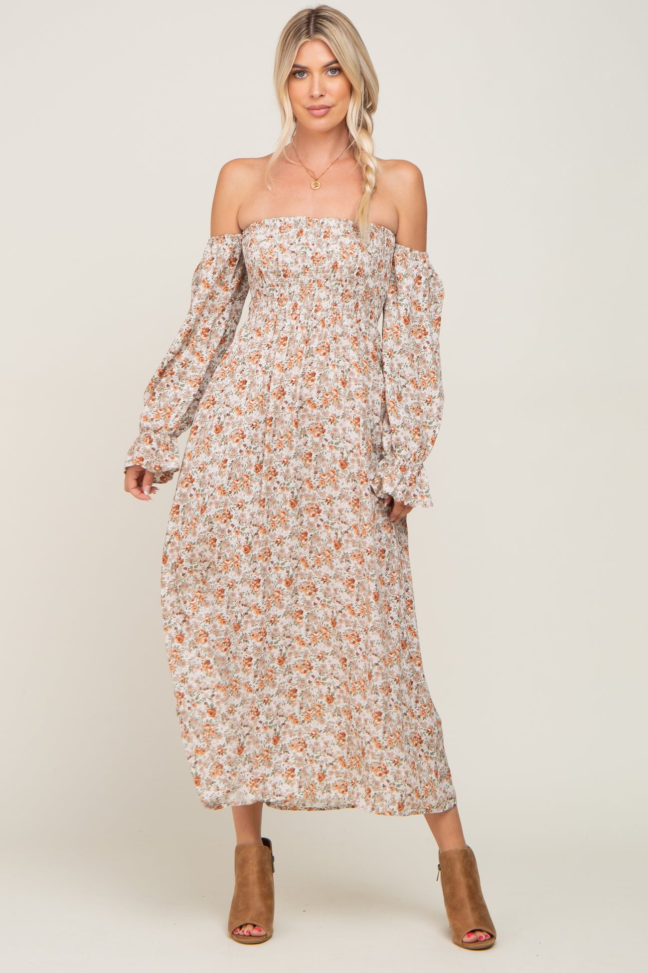 woman wearing a floral off-the-shoulder maxi dress with long sleeves and a smocked bodice, paired with brown heeled sandals