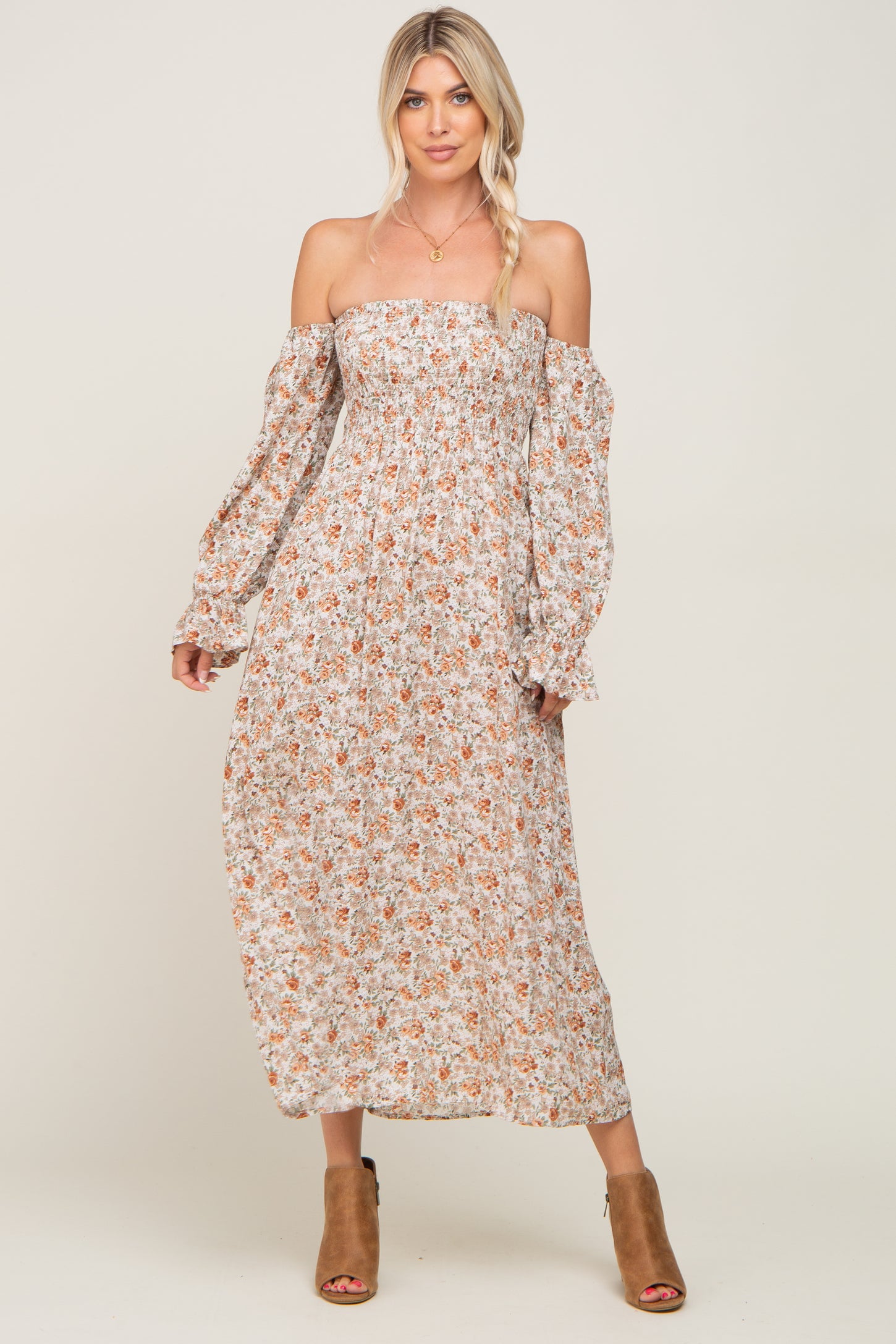 woman wearing a floral off-the-shoulder maxi dress with long sleeves and a smocked bodice, paired with brown heeled sandals