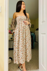 woman wearing a floral off-the-shoulder maternity dress with a baby bump visible, standing in a bright room