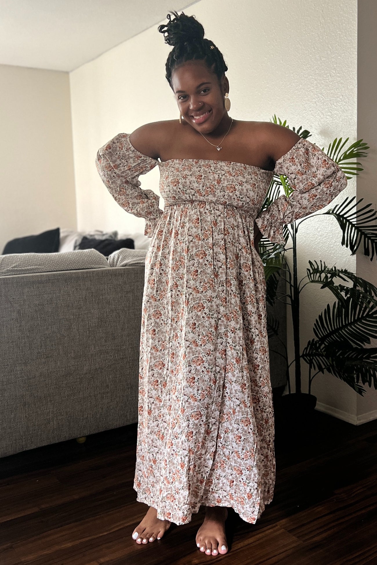 woman wearing a floral off-the-shoulder maxi dress with long sleeves and a flowy skirt, posing with a smile indoors