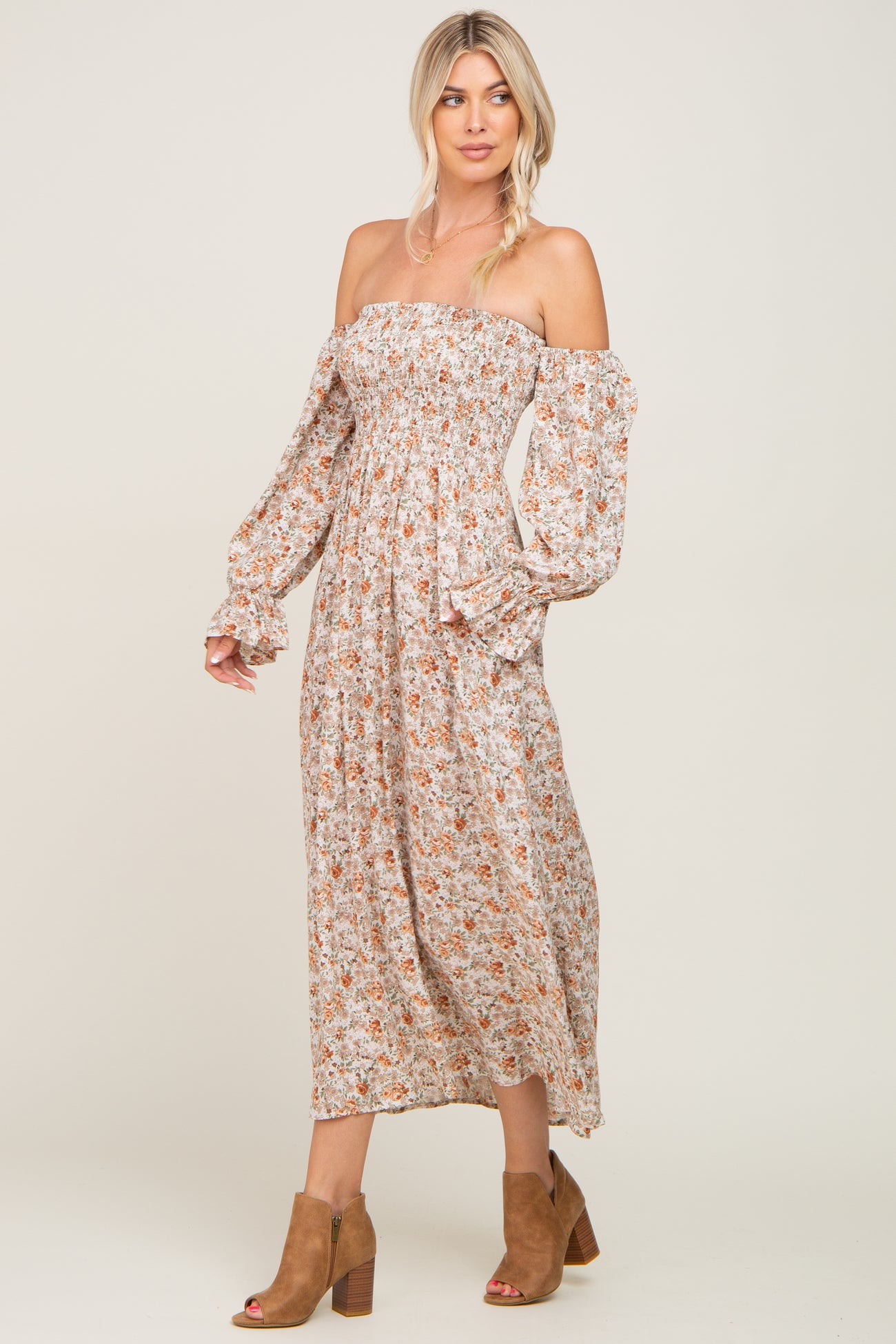 woman wearing a floral off-the-shoulder maxi dress with long sleeves and a fitted bodice, paired with brown ankle boots