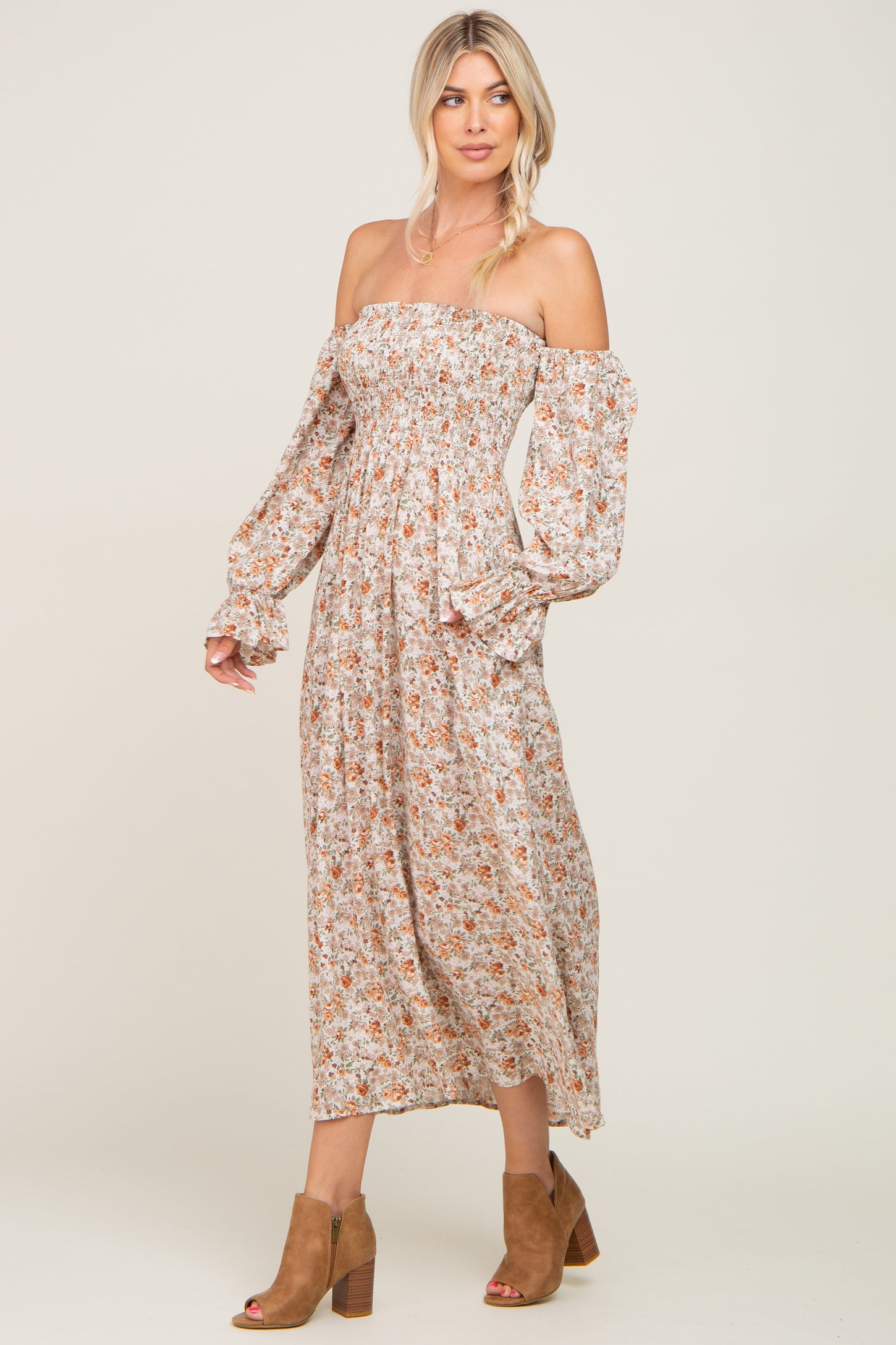woman wearing a floral off-the-shoulder maxi dress with long sleeves and a fitted bodice, paired with brown ankle boots