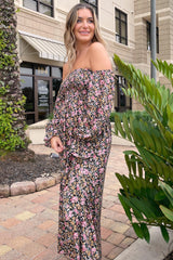 woman wearing a black floral off-the-shoulder maternity dress with long sleeves and a relaxed fit, standing outdoors