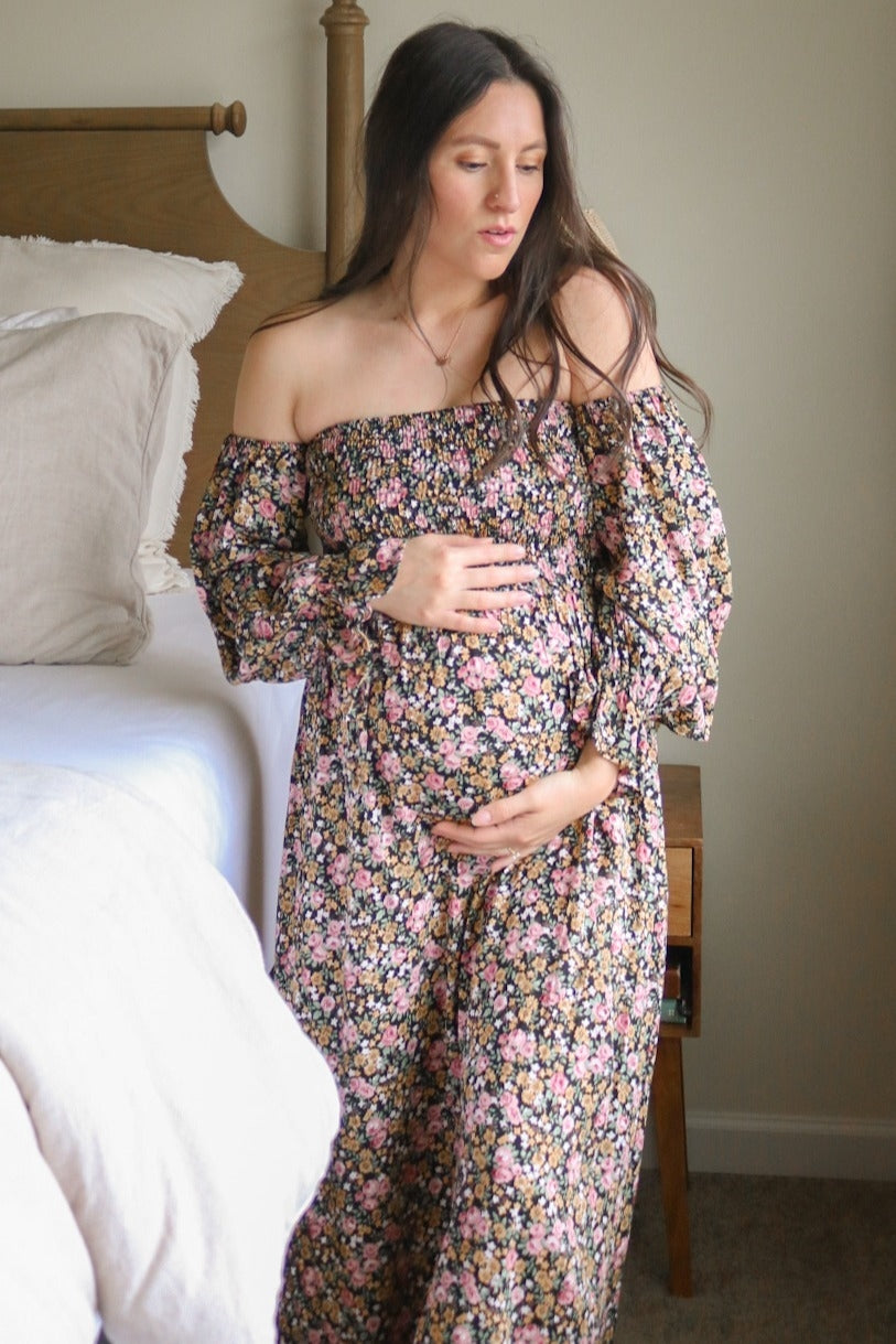 woman wearing a floral off-the-shoulder maternity dress and holding her baby bump
