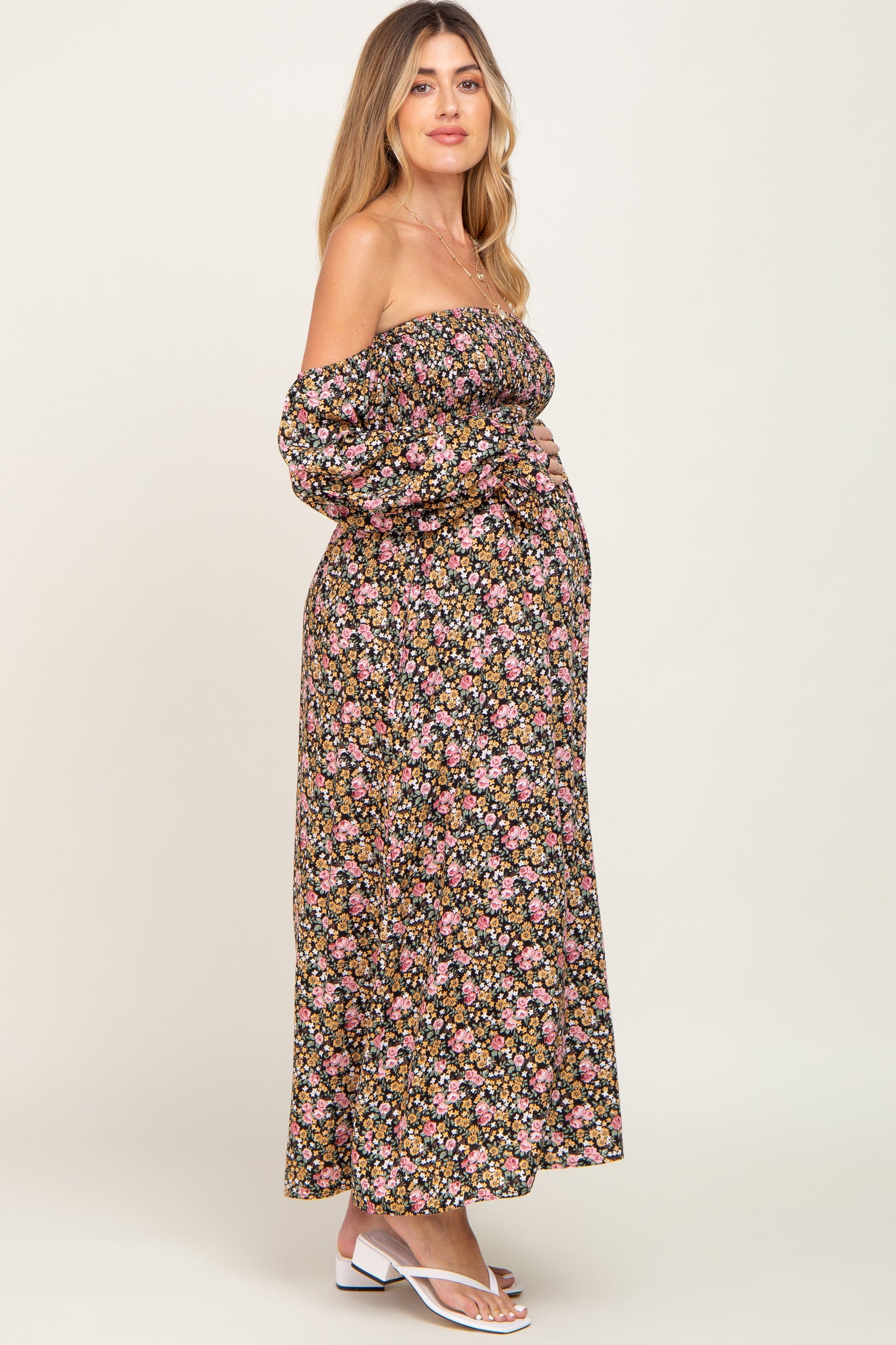 woman wearing a black off-the-shoulder floral maternity dress and posing with her baby bump