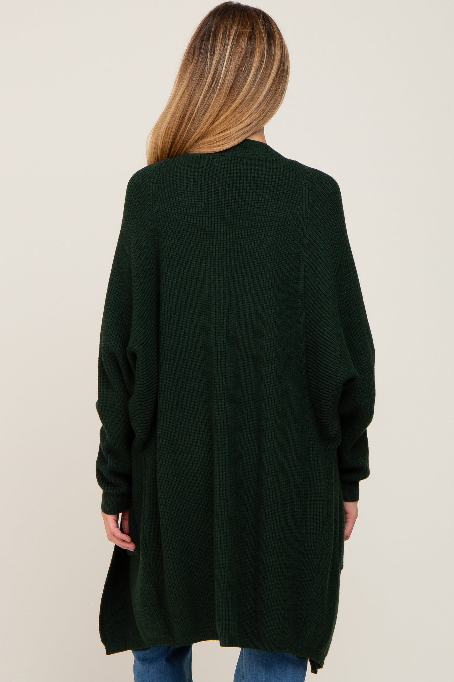 woman wearing a long green maternity cardigan, view from the back, with loose fit and ribbed texture