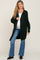 woman wearing a dark green maternity cardigan over a white top, with a visible baby bump, paired with blue flared jeans