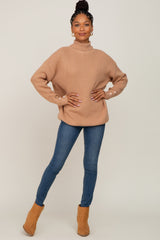woman wearing a beige chunky knit sweater with button details and blue skinny jeans, standing in brown ankle boots