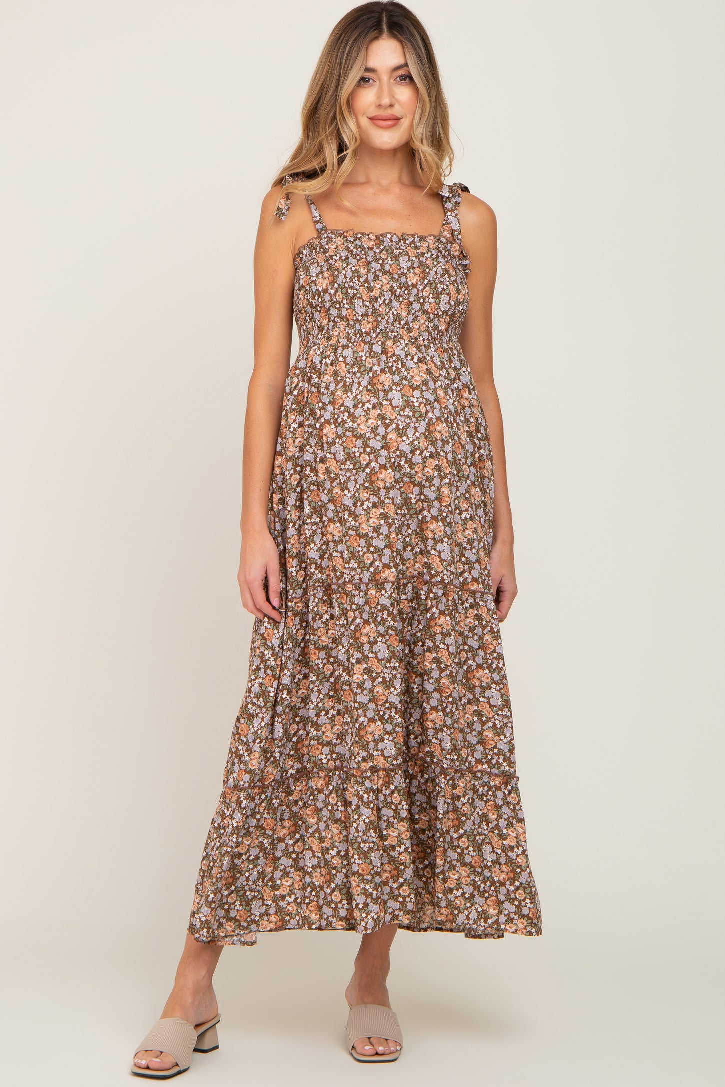 woman wearing a brown floral maternity maxi dress with adjustable straps and a ruffled hem, showcasing her baby bump