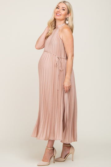 woman wearing a light pink pleated maternity dress with a halter neck and tie waist, showing her baby bump