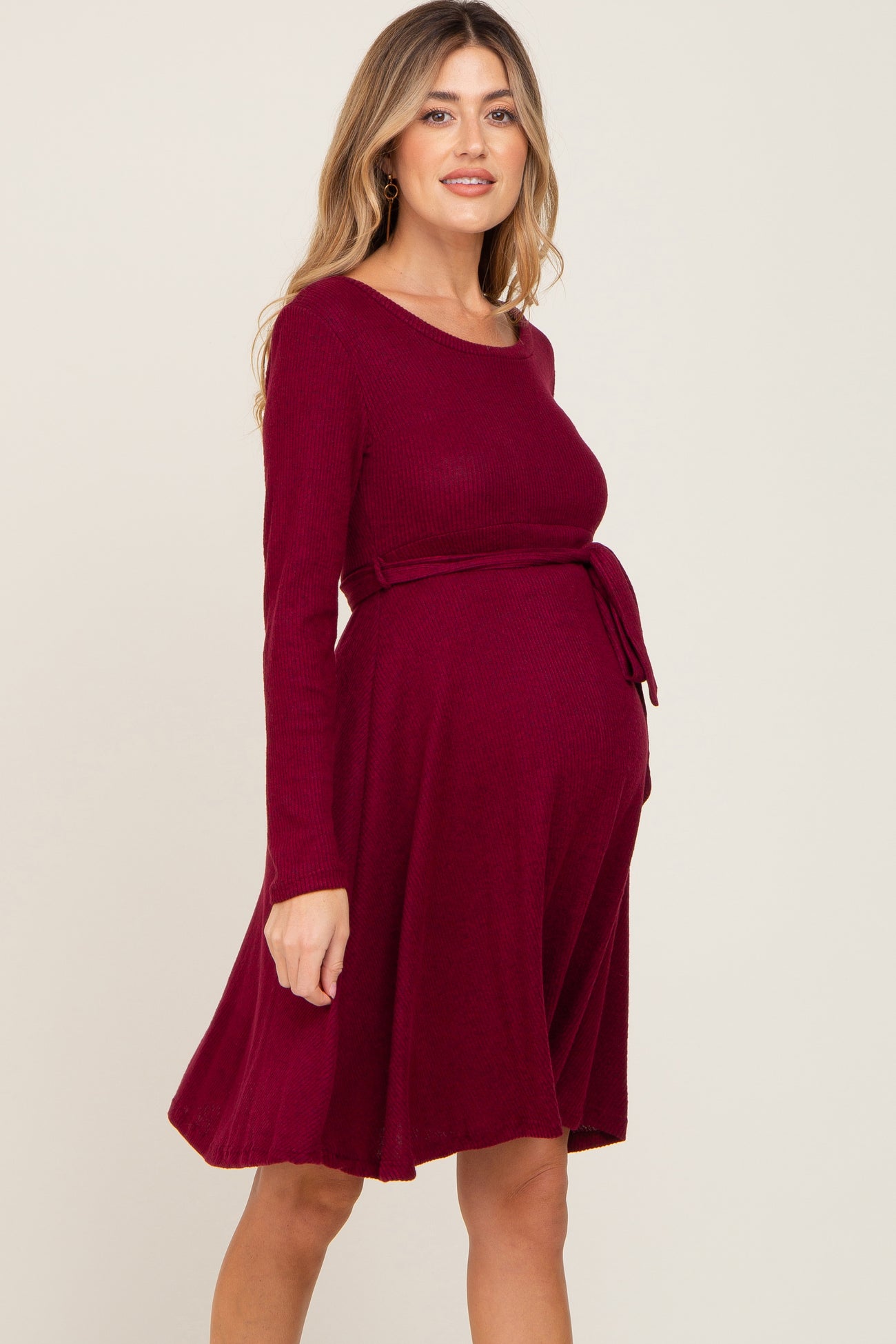 woman wearing a burgundy long sleeve maternity dress with a tie waist and a visible baby bump
