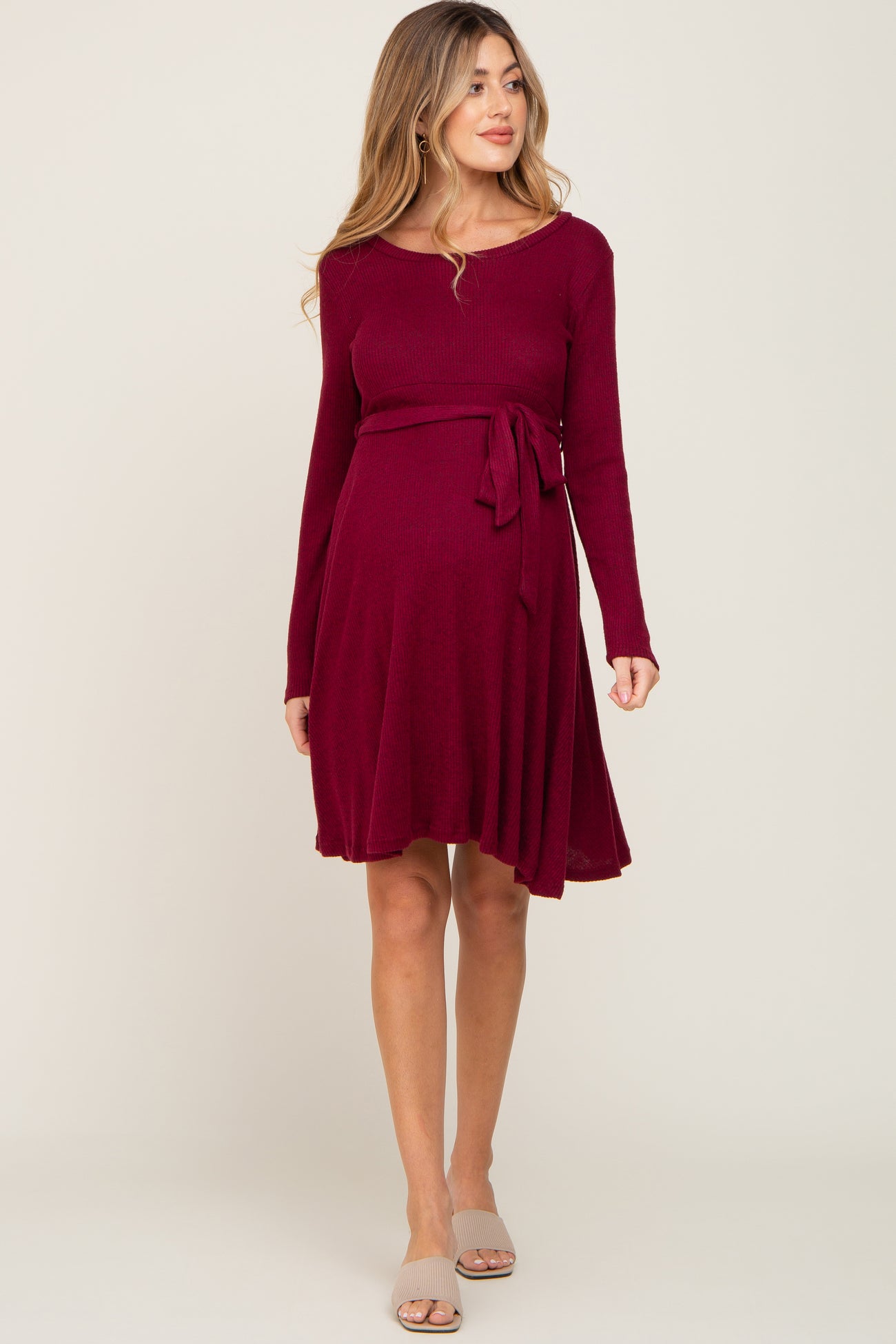 woman wearing a burgundy long sleeve maternity dress with a tie waist and flowing skirt, showing baby bump