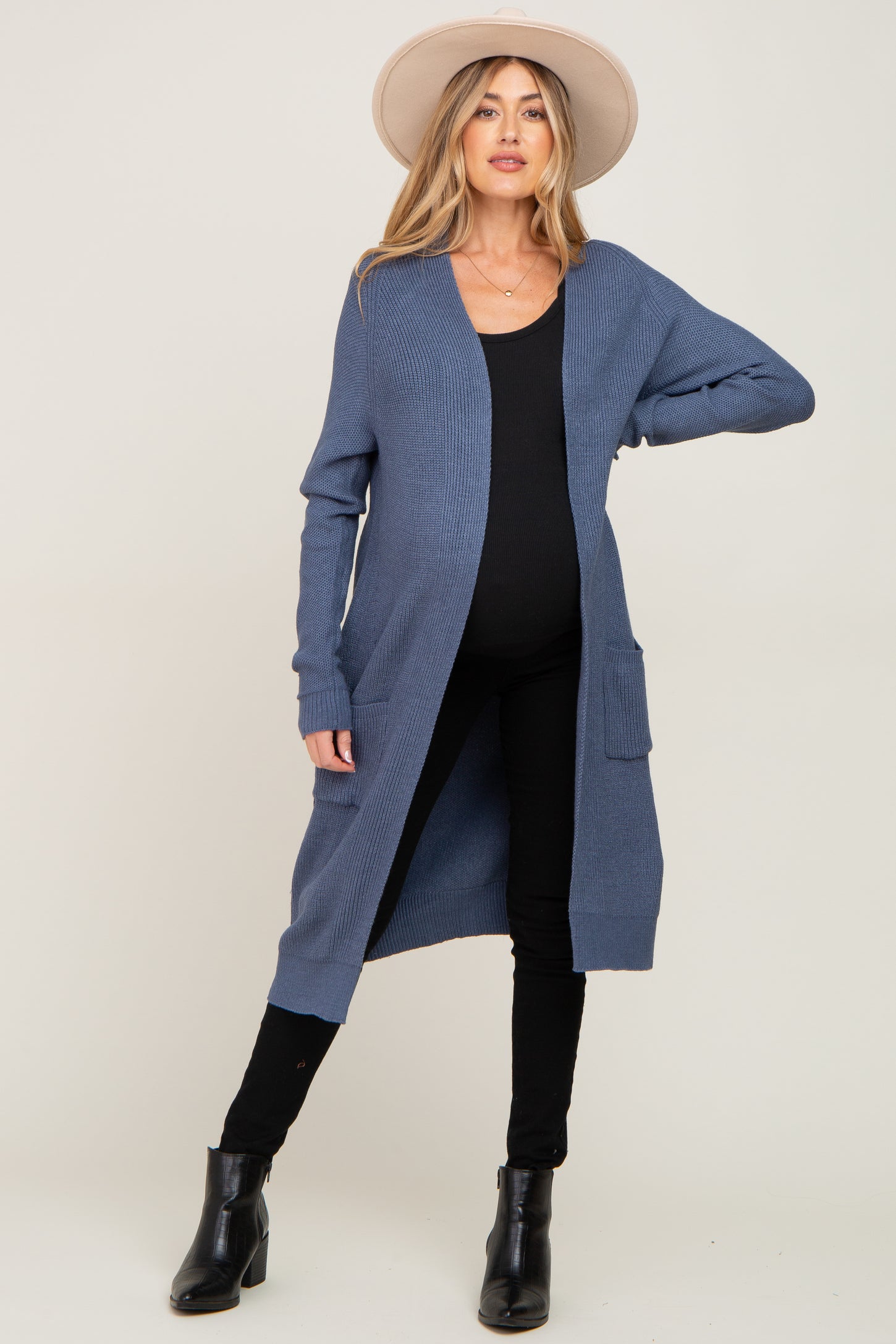 woman wearing a navy blue long sleeve maternity cardigan with pockets and black pants, showing her baby bump