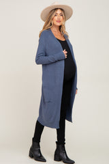 woman wearing a blue long sleeve maternity cardigan over a black top and jeans, with a visible baby bump