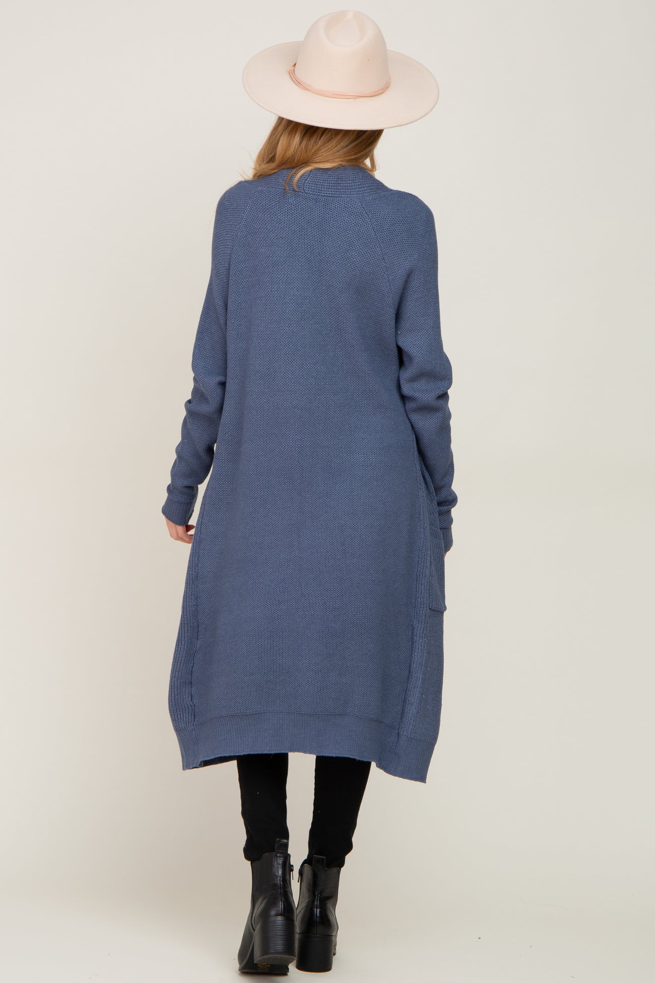 woman wearing a long blue maternity cardigan with a loose fit and side pockets, facing away from the camera