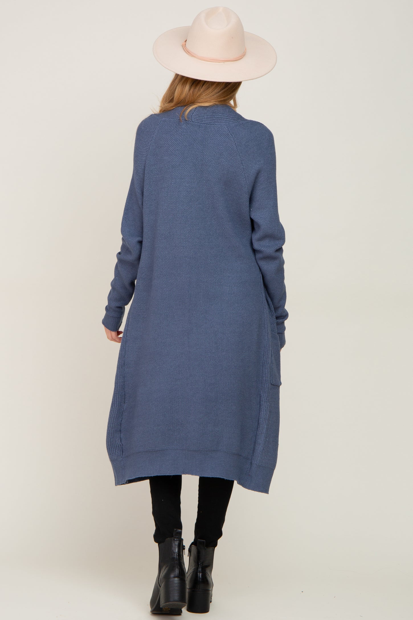 woman wearing a long blue maternity cardigan with a loose fit and side pockets, facing away from the camera