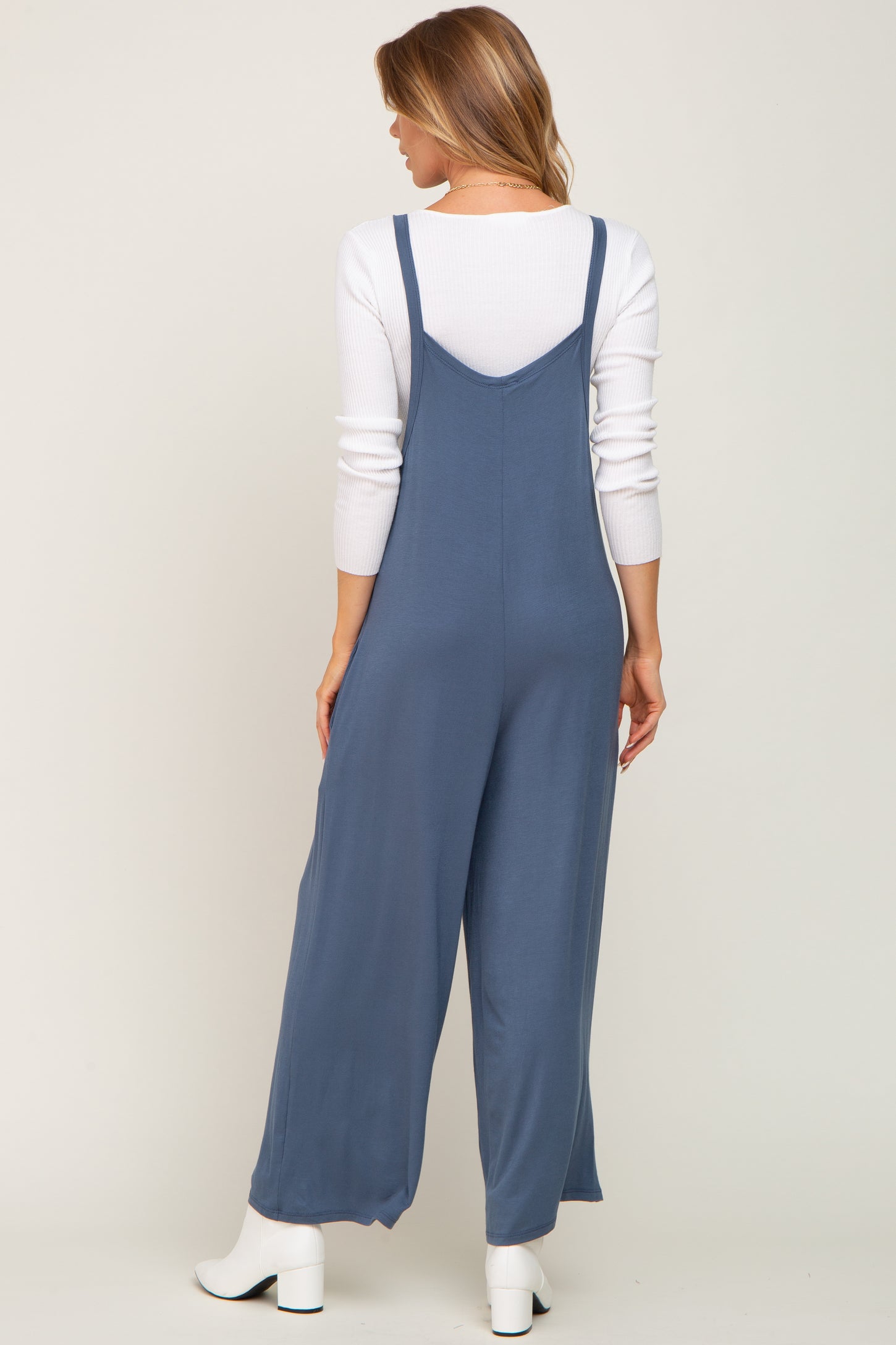 Woman from behind wearing a blue wide leg jumpsuit over a white long sleeve shirt and white boots