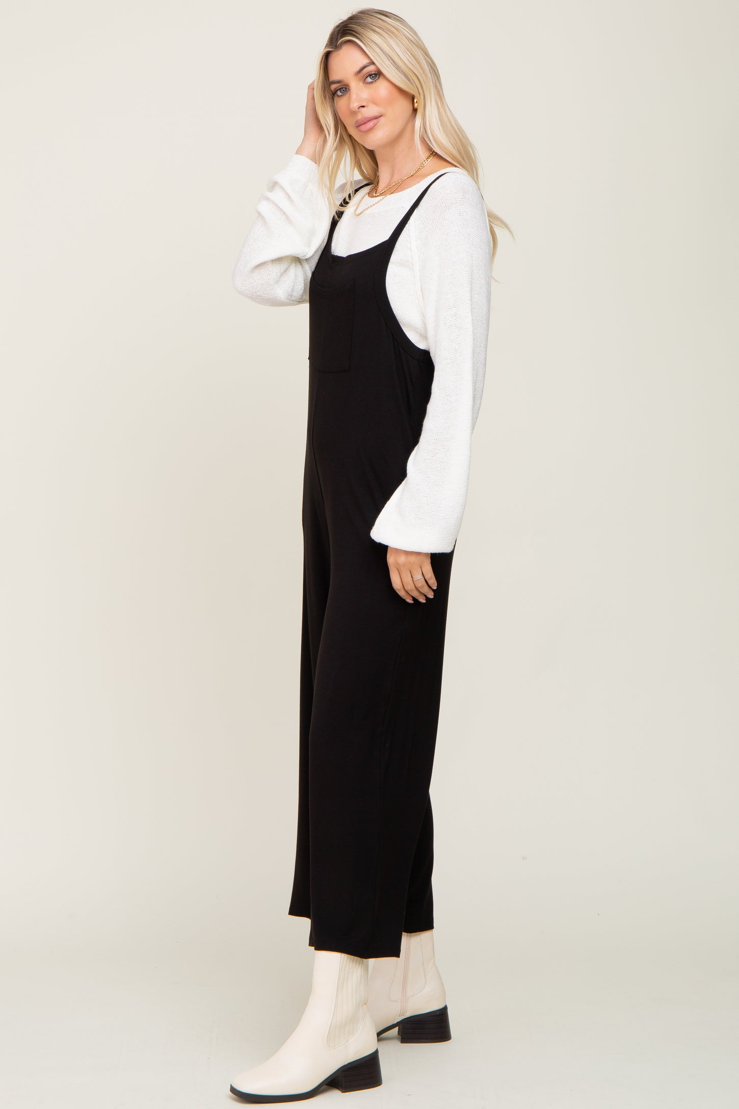woman wearing a black jumpsuit with a square pocket and long white sleeves, standing sideways with one hand in her hair