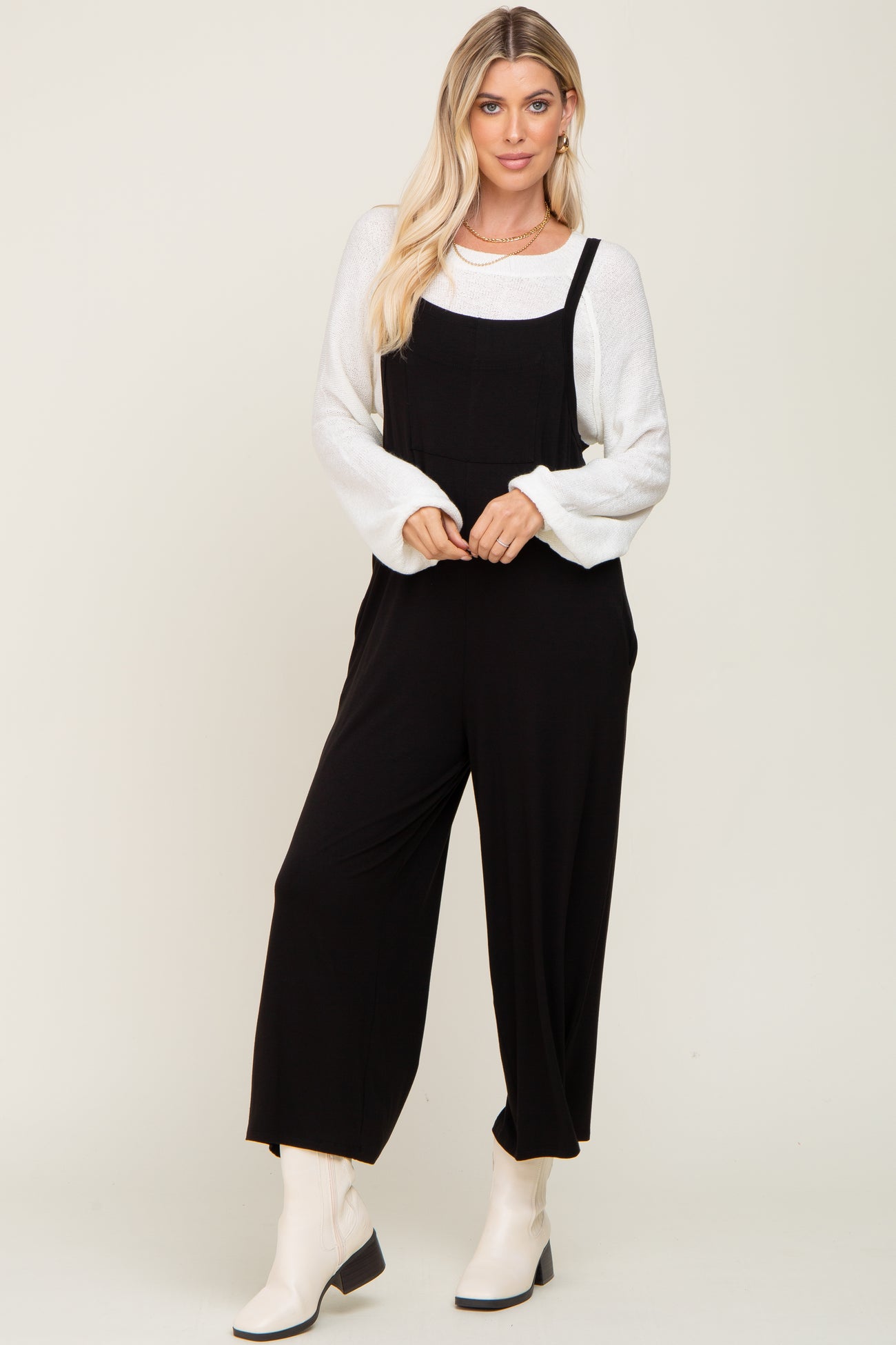 woman wearing a black jumpsuit over a white sweater and white ankle boots
